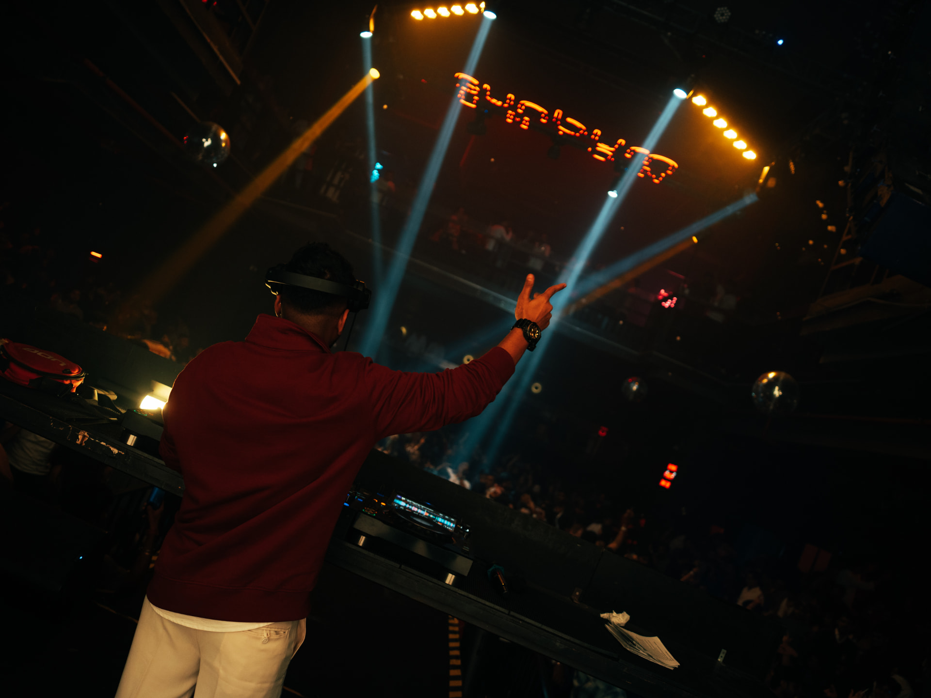 DJ in a maroon hoodie pointing toward the crowd from behind the decks