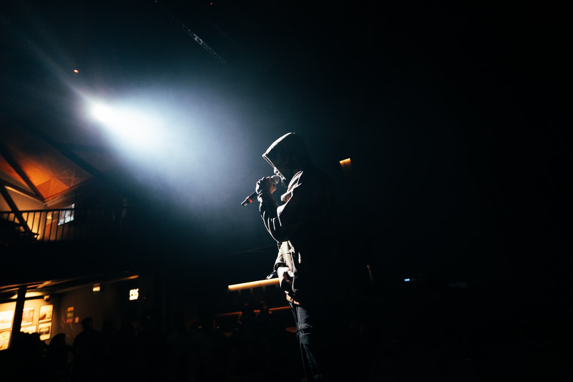 Rapper in a hoodie performing into a microphone under a bright spotlight