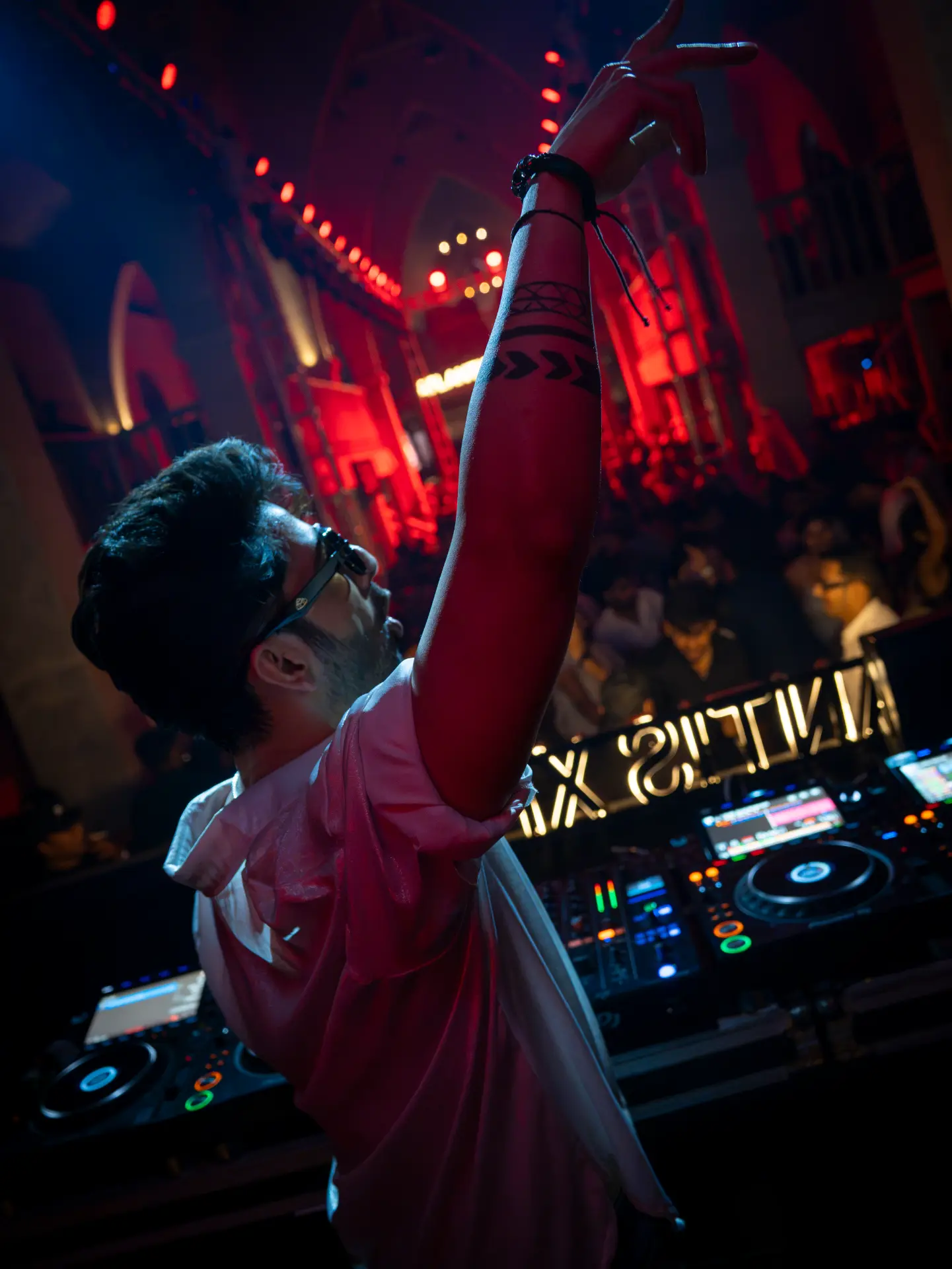 DJ raising his arm above the decks under red club lighting