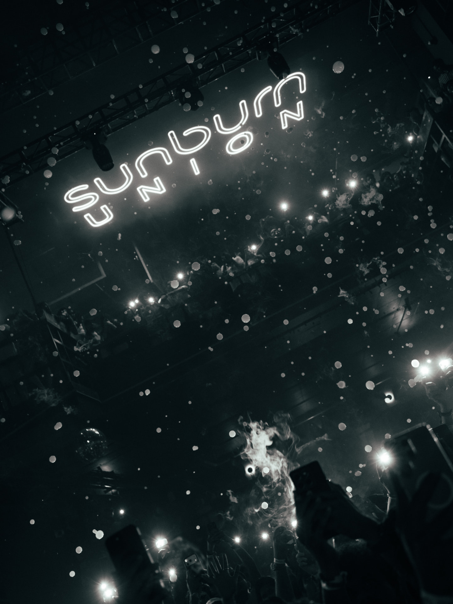 Sunburn Union sign glowing above a crowd holding up phone lights