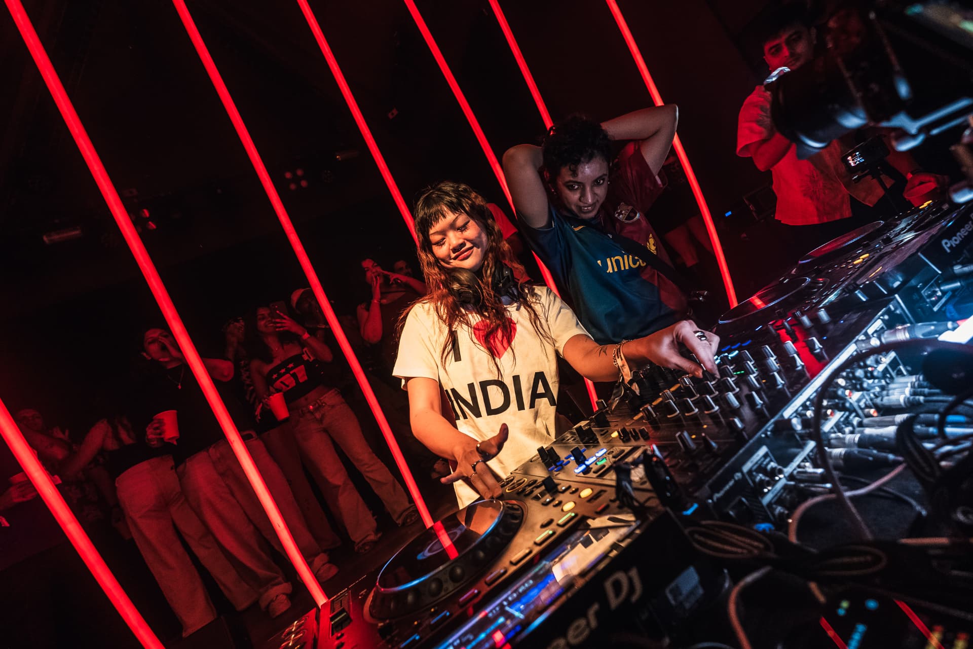 Two DJs mixing at a booth wrapped in red neon light strips