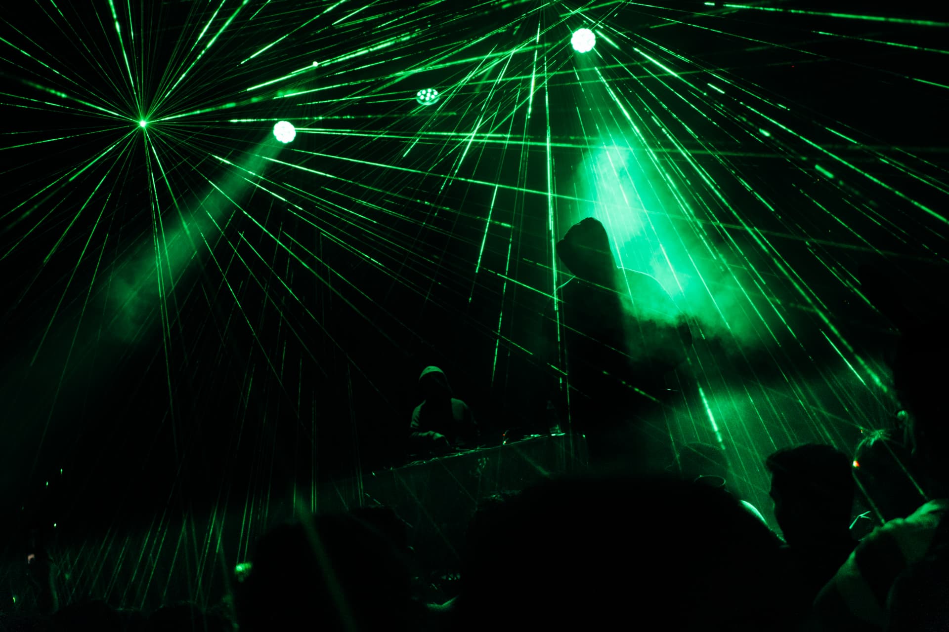 Green laser beams cutting through haze above a DJ and the crowd