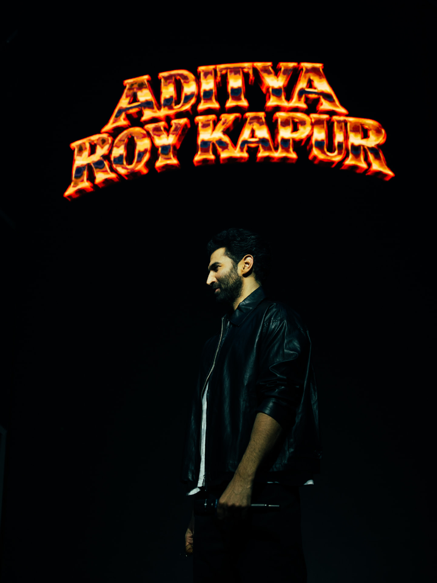 Aditya Roy Kapur standing beneath a fiery marquee of his name
