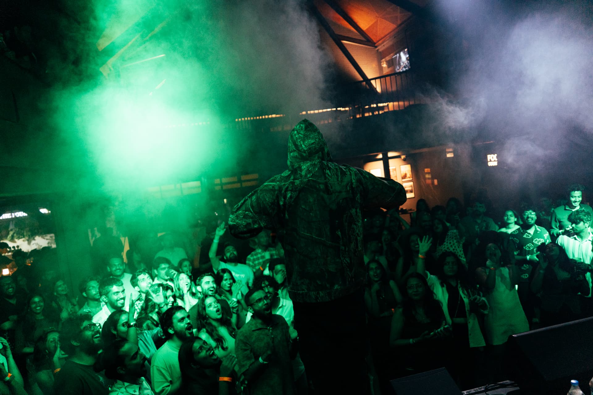 Performer facing a cheering crowd through drifting green smoke